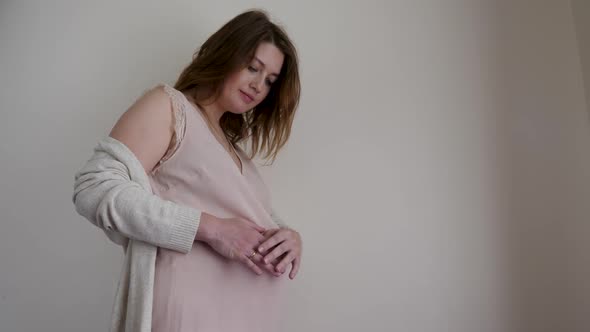 Pregnant Woman in a Nightie Stands at the Wall of the House and Strokes