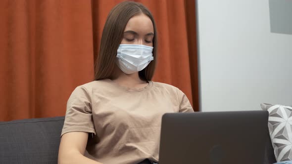 Young Woman Wearing Face Mask While Working on a Computer at Home During Virus Epidemic