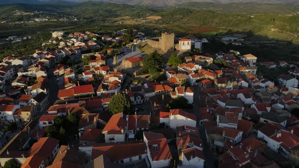 A drone tilts over a water tower to show Belmonte castle as birds fly by.