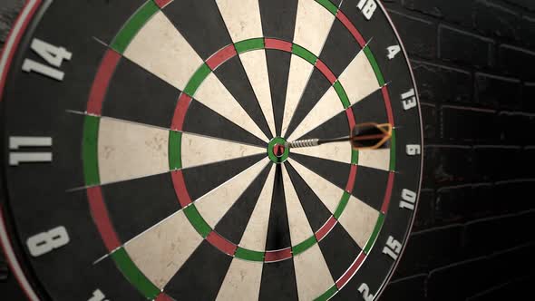 Darts arrow hitting in the bullseye of the dartboard hanging on the dark wall.