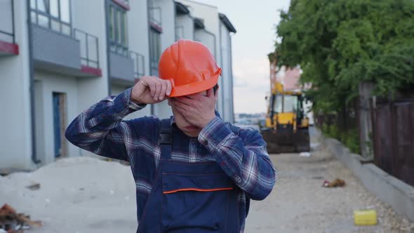 Man Takes Off Orange Helmet and Crosses Hands