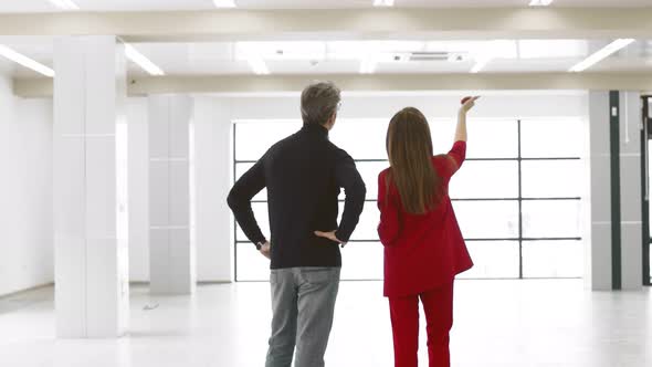 Businesswoman in business suit tells gray-haired Caucasian man and points something