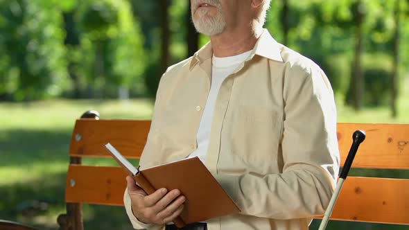 Blind Man Reading Book in Braille Sitting on Bench in Park, Social Adaptation