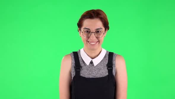 Portrait of Funny Girl in Round Glasses Is Laughing Shyly While Looking at Camera. Green Screen