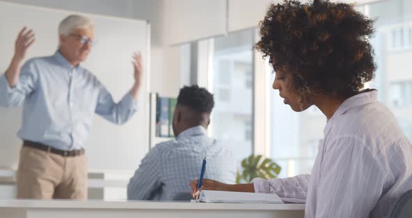 Young African Woman Sitting at Desk Listening to Professor and Writing Down Notes / Videohive