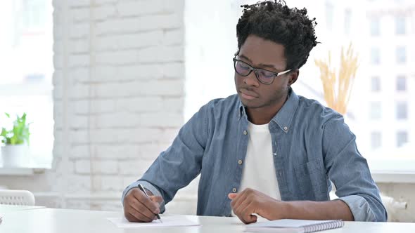 Young African Man Writing on Document in Office