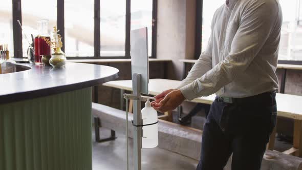 Caucasian man working at a bar, using hand sanitising gel dispenser