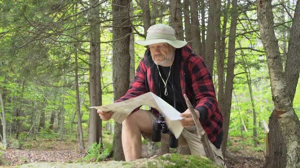 An older man looking at a map while hiking in a scenic forest in the mountains