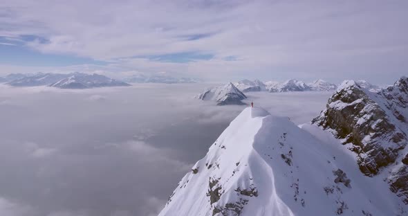 Aerial drone view of a mountain climber skier on the peak summit top of a snow covered mountain