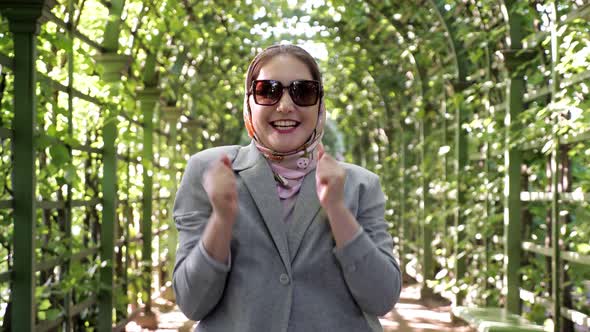 Woman in a Scarf and Sunglasses Experiences Unbridled Joy in a Garden Arch