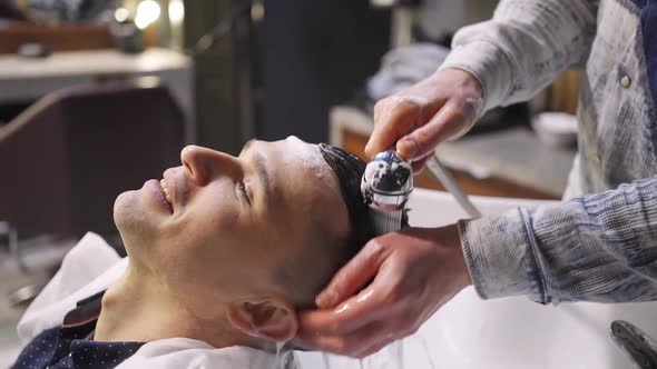 a Hairdresser Washes the Hair of a Brunette Man in a Barbershop