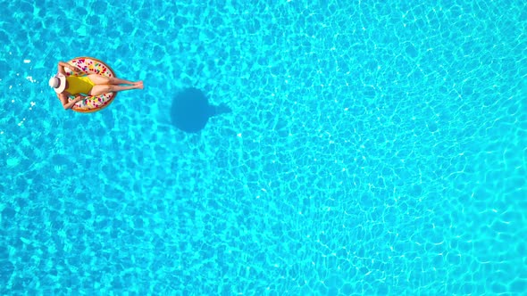 Aerial View of a Woman in Yellow Swimsuit Lying on a Donut in the Pool alt