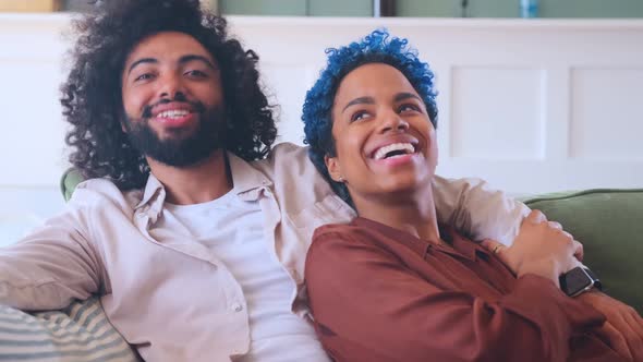 Young Multiethnic Cheerful Couple Free From Racial Prejudice Sits on Sofa