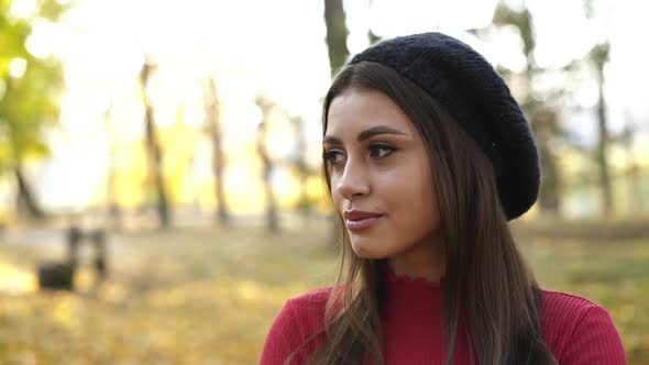 Cheerful Brunette in a Cap Posing Looking and Smiling at Camera in Park