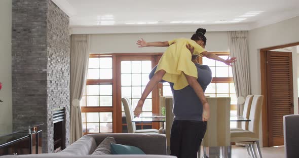 Happy african american father lifting up daughter and having fun in living room