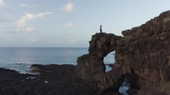 Aerial view of a person standing alone on top of a natural arch along the coastline, Mauritius.