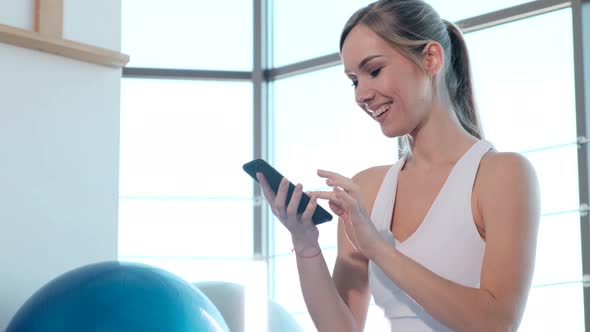 Fitness girl relaxing with cellphone in gym