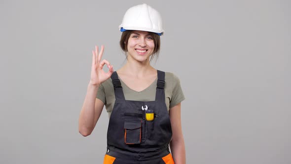 Portrait of Caucasian Forewoman in Helmet and Jumpsuit Smiling and Showing Ok Sign While Working on