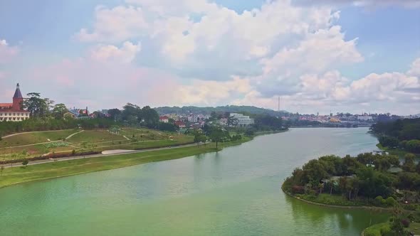 Camera Moves Over Large Lake with City and Green Forest on Banks