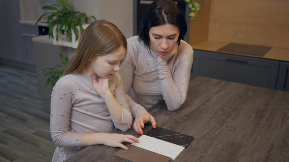 Joyful Caucasian Woman and Girl Sitting at Table in Store Choosing Tiles Design and Color Looking at