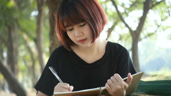 young asian woman writing into her diary in park. Happy hipster young asian woman work on notebook.