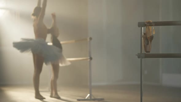 Golden Pointes Hanging on Barre with Blurred Teacher Explaining Ballet Movement for Student at