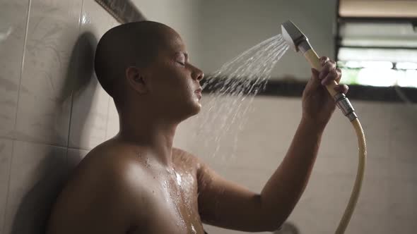 Sick and weak bald Asian girl is bathing with hand shower in bathroom is very upset and crying