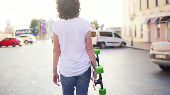 Back View of a Woman Walking in the Old City Street Holding Her Trendy Stylish Longboard with