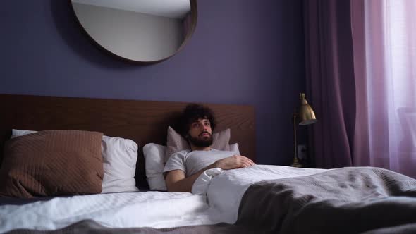 Happy Sleeping Young Man Opening Eyes Waking Up and Stretching in Morning Sitting on Bed