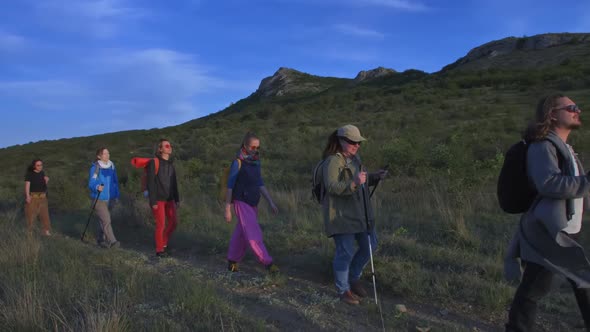 a Company of Tourists with Backpacks Walk Along the Trail Against the Mountains and Blue Sky