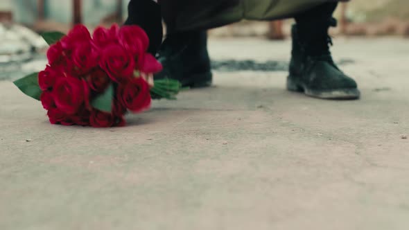 Man Leans Bunch of Red Flowers on the Ground