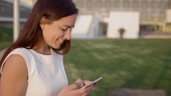 Side View of Smiling Redhead Woman Typing on Smartphone