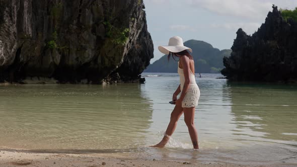 Woman In Sun Hat Touching Sea Water On Hidden Beach