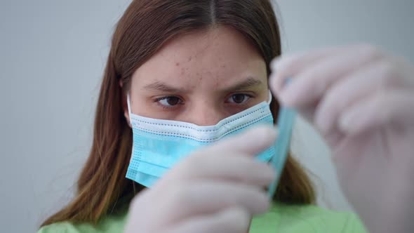 Headshot Front View of Focused Young Lab Assistant in Face Mask and Uniform Examining Test Tube