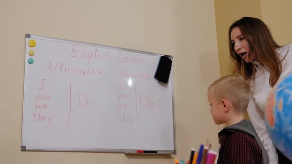 Closeup of a Small Boy with a Teacher Near the Blackboard at School