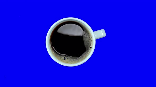 Small Coffee Cup with White Coffee on Saucer Rotating on Blue Screen, Loop, Top View. Alpha Channel.