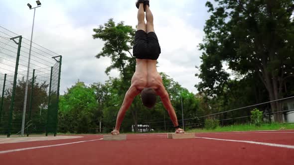 A Shirtless Athlete is Standing Upside Down Leaning on Special Racks on Race Track Outdoors