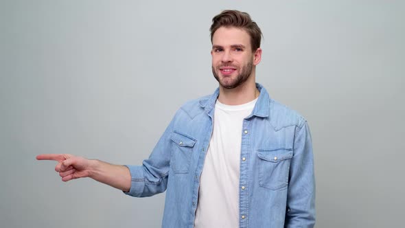 Young caucasian man smiling and pointing aside, showing something at blank space