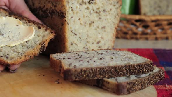 Close up shot of woman's hands spreading butter with a kitchen knife on a crispy slice of homemade b