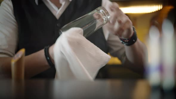 The Bartender in the Pub or Restaurant Wipes a Glass with a Towel