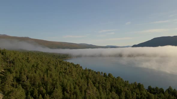 Aerial flight over foggy alpine landscape and calm lake