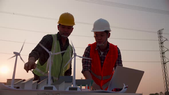 Asian engineer discussion about home solar cell farm and wind turbine model in construction site