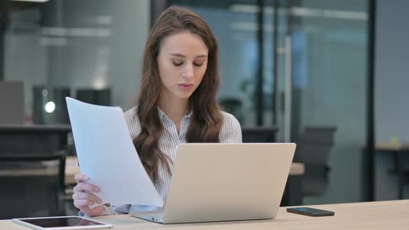 Young Businesswoman With Laptop Reading Documents at Work