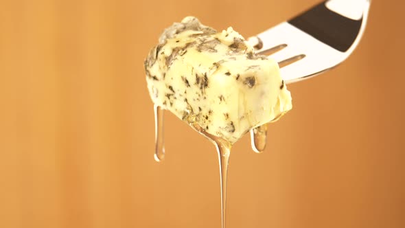 Liquid Organic Honey Dripping on a Fork with Dorbly Cheese on a Light Background