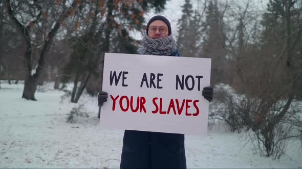 Male Protester Holding a Sign with the Words We Are Not Your Slaves in a Park