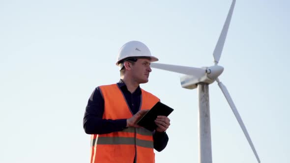 Engineer Caucasian Appearance, Stands Near the Windmill with the Tablet in His Hands and Looks