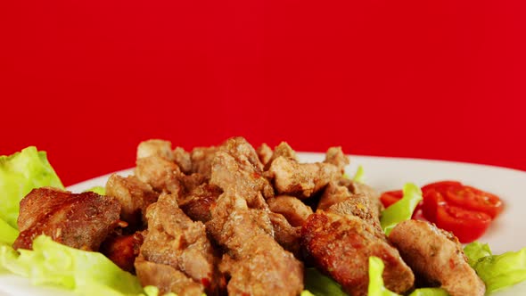 Pieces of meat in a white plate on lettuce leaves and cherry tomatoes