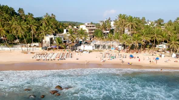 Aerial drone pan along busy Sri Lank beach at sunset golden hour. Mirissa Beach bar, Sri Lanka