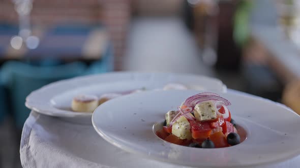 Closeup Greek Salad on White Plate on Tray in Hand of Unrecognizable Waiter Walking in Slow Motion