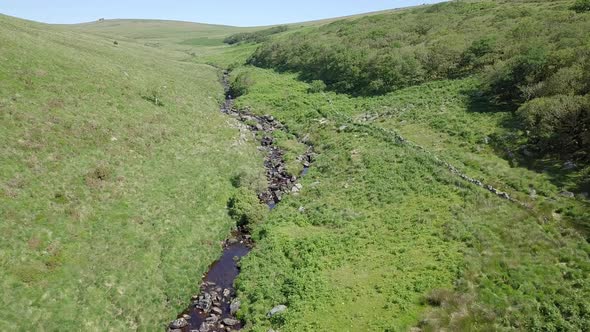 Wide aerial shot tracking forward, with wistmans wood, a river and grassy moorland setting the scene